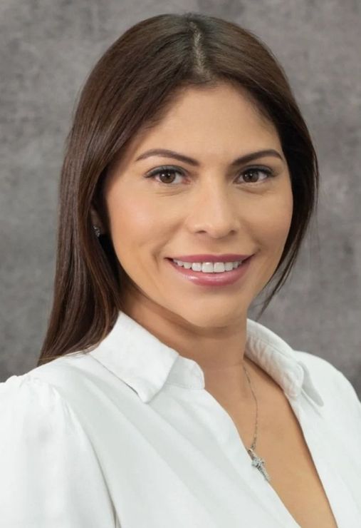 Woman with brown hair smiles, wearing a white collared shirt. Gray background.