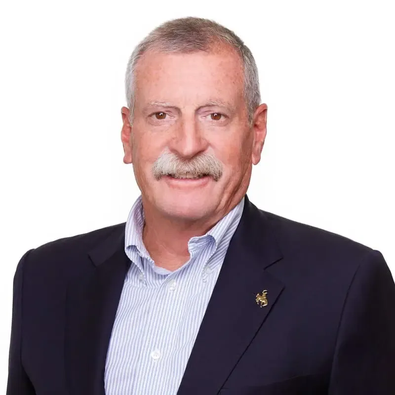 Man with mustache wearing a blue blazer over a light blue collared shirt; smiling.