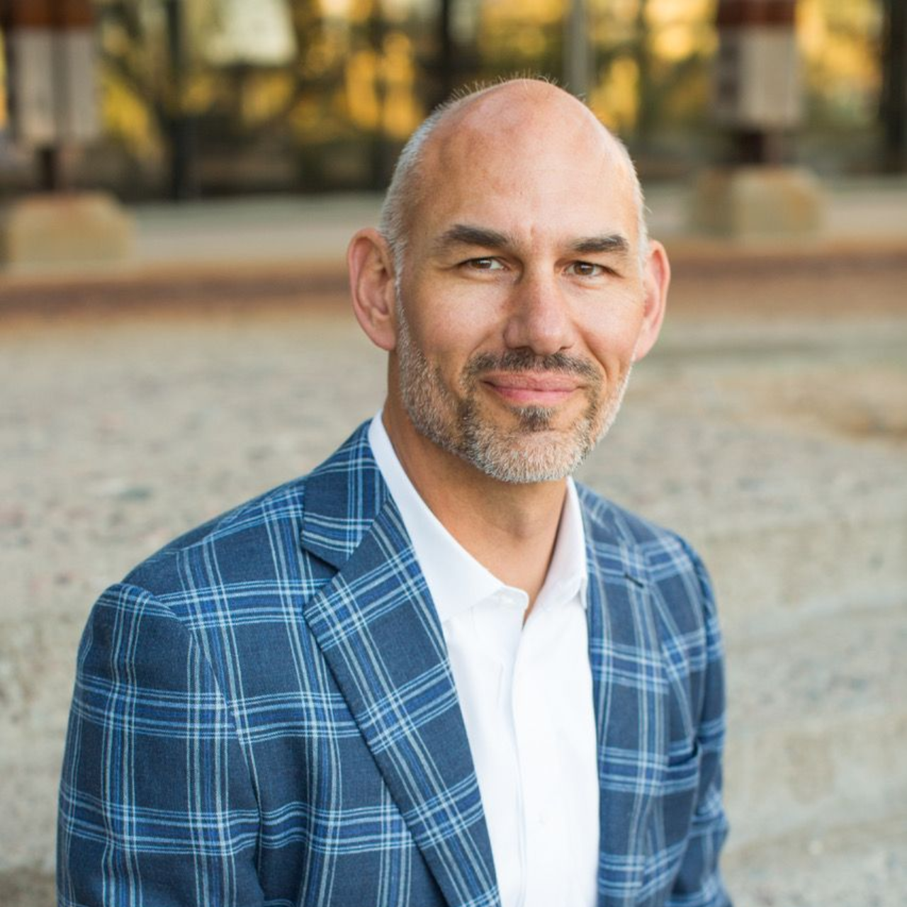 Man in blue plaid blazer and white shirt, smiling outdoors.
