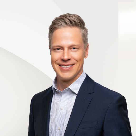 Man in blue suit smiling, light-colored hair, white and light blue striped shirt, white background.