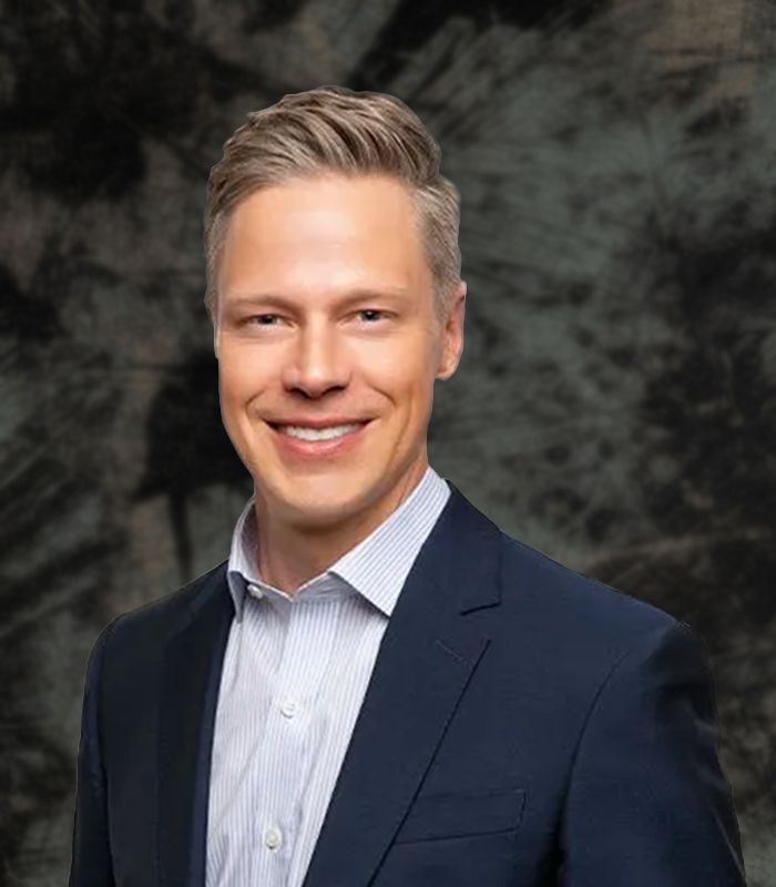 Man in blue suit smiling, light-colored hair, white and light blue striped shirt, white background.