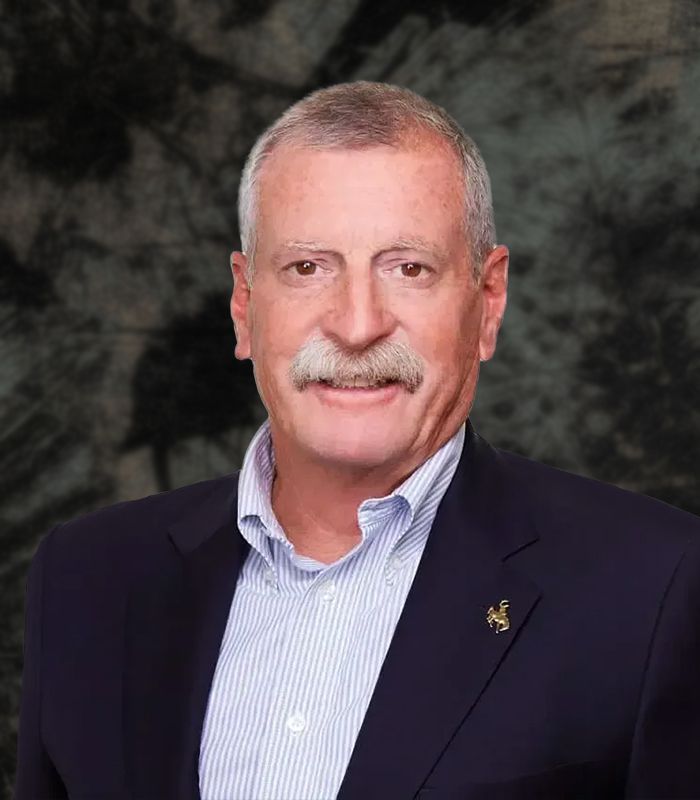 Man with mustache wearing a blue blazer over a light blue collared shirt; smiling.