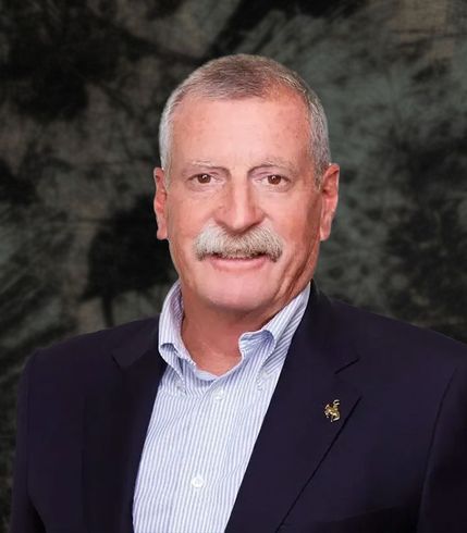 Man with mustache wearing a blue blazer over a light blue collared shirt; smiling.