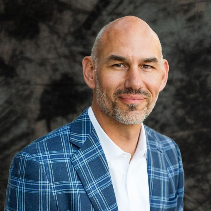 Man in blue plaid blazer and white shirt, smiling outdoors.