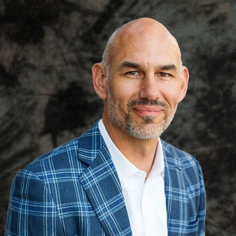 Man in blue plaid blazer and white shirt, smiling outdoors.
