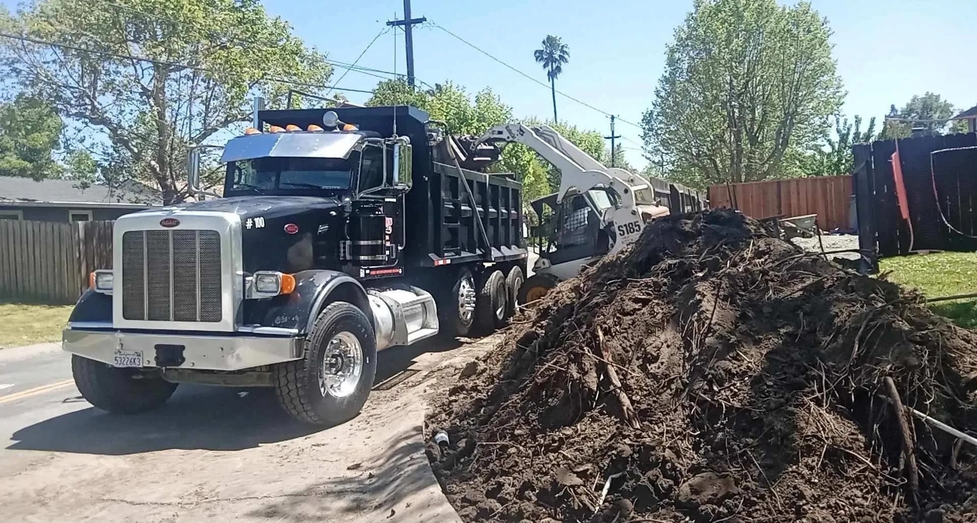 Dump truck unloading soil onto a dirt field under a cloudy sky