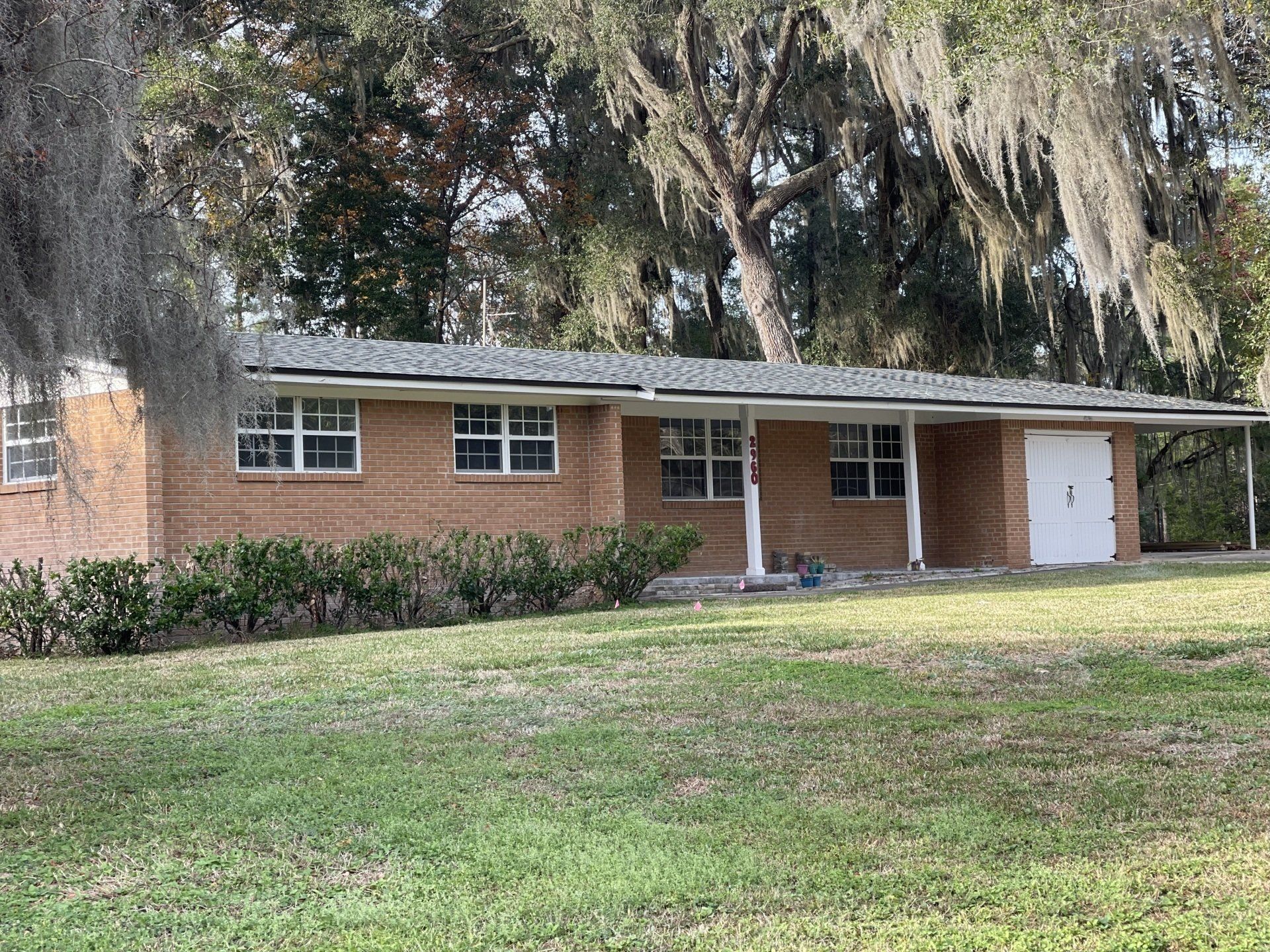 A brick house with a porch and trees in the background.