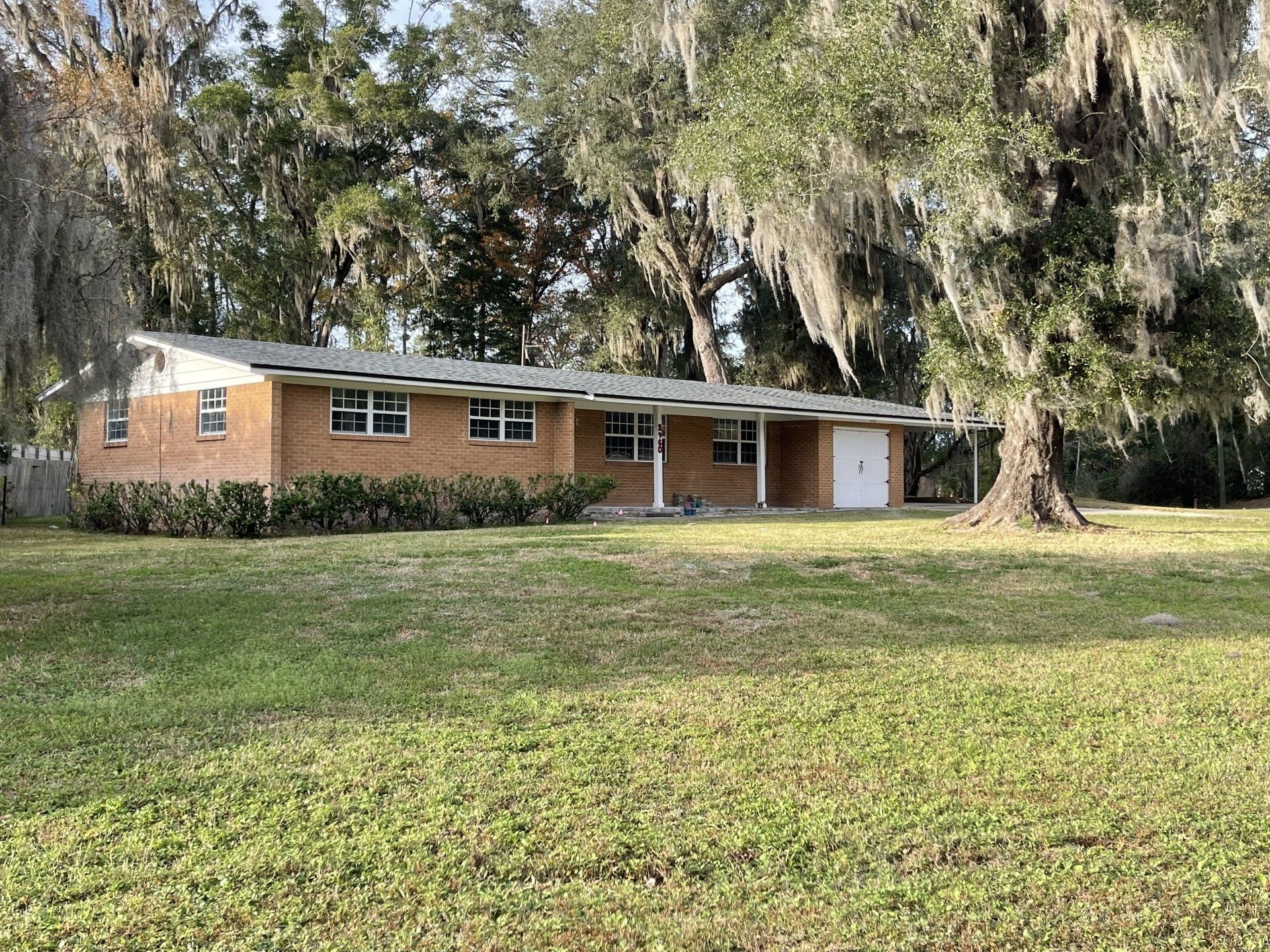 A brick house is sitting on top of a lush green field surrounded by trees.