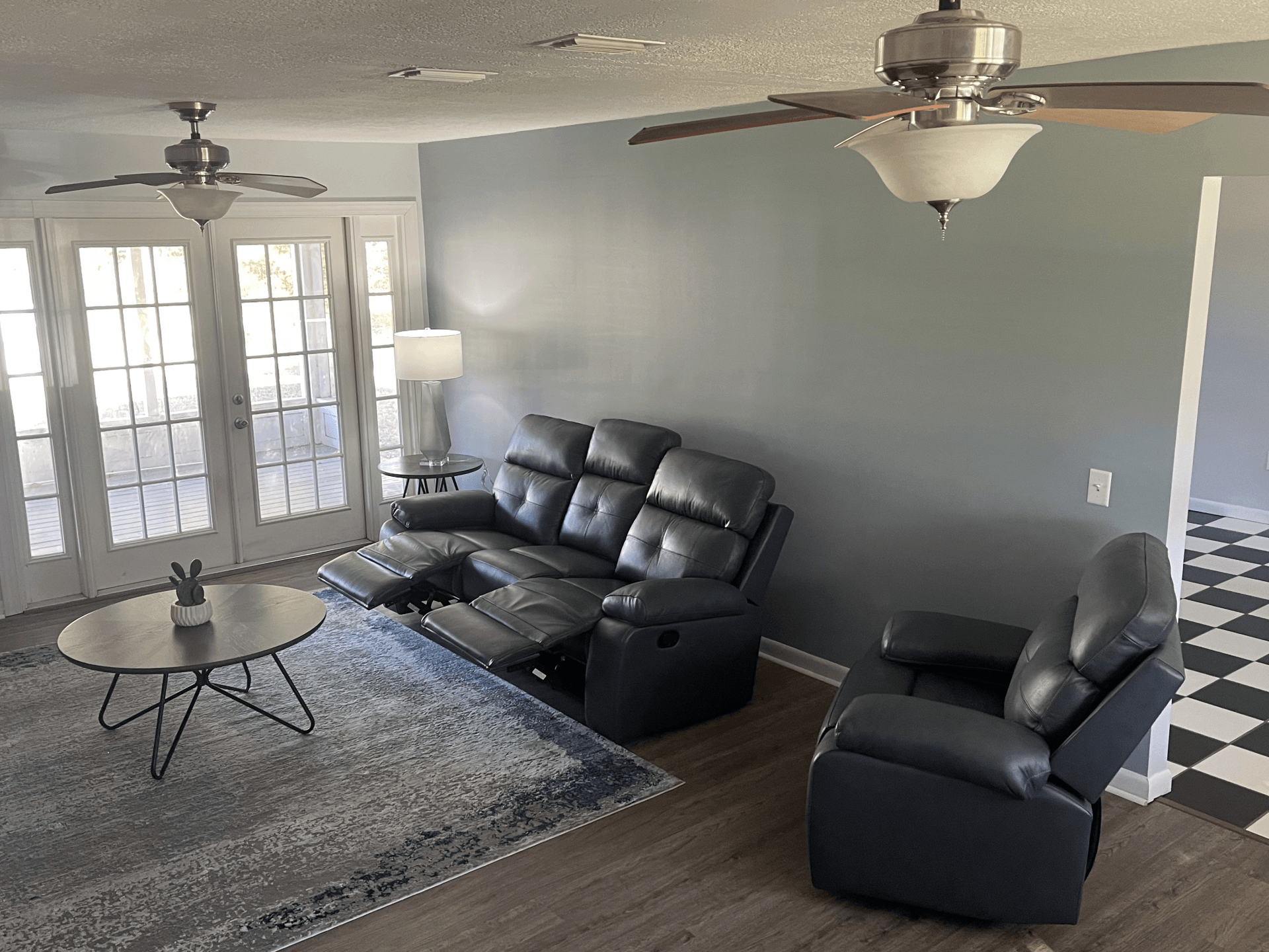A living room with a couch , chair , coffee table and ceiling fan.