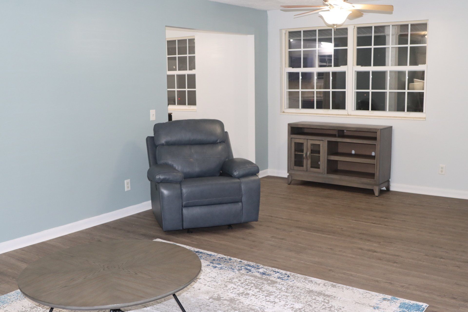 A living room with a chair , table , and ceiling fan.