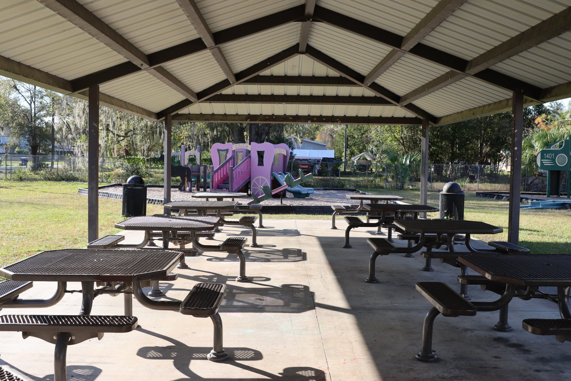 A picnic shelter with tables and benches in a park with a playground in the background.