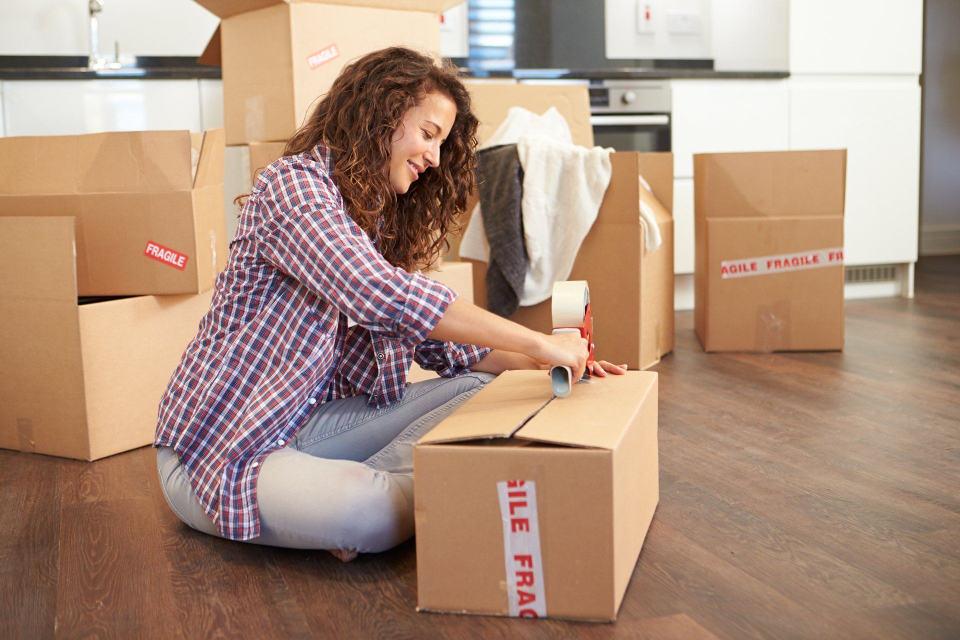 A woman is sitting on the floor packing boxes.