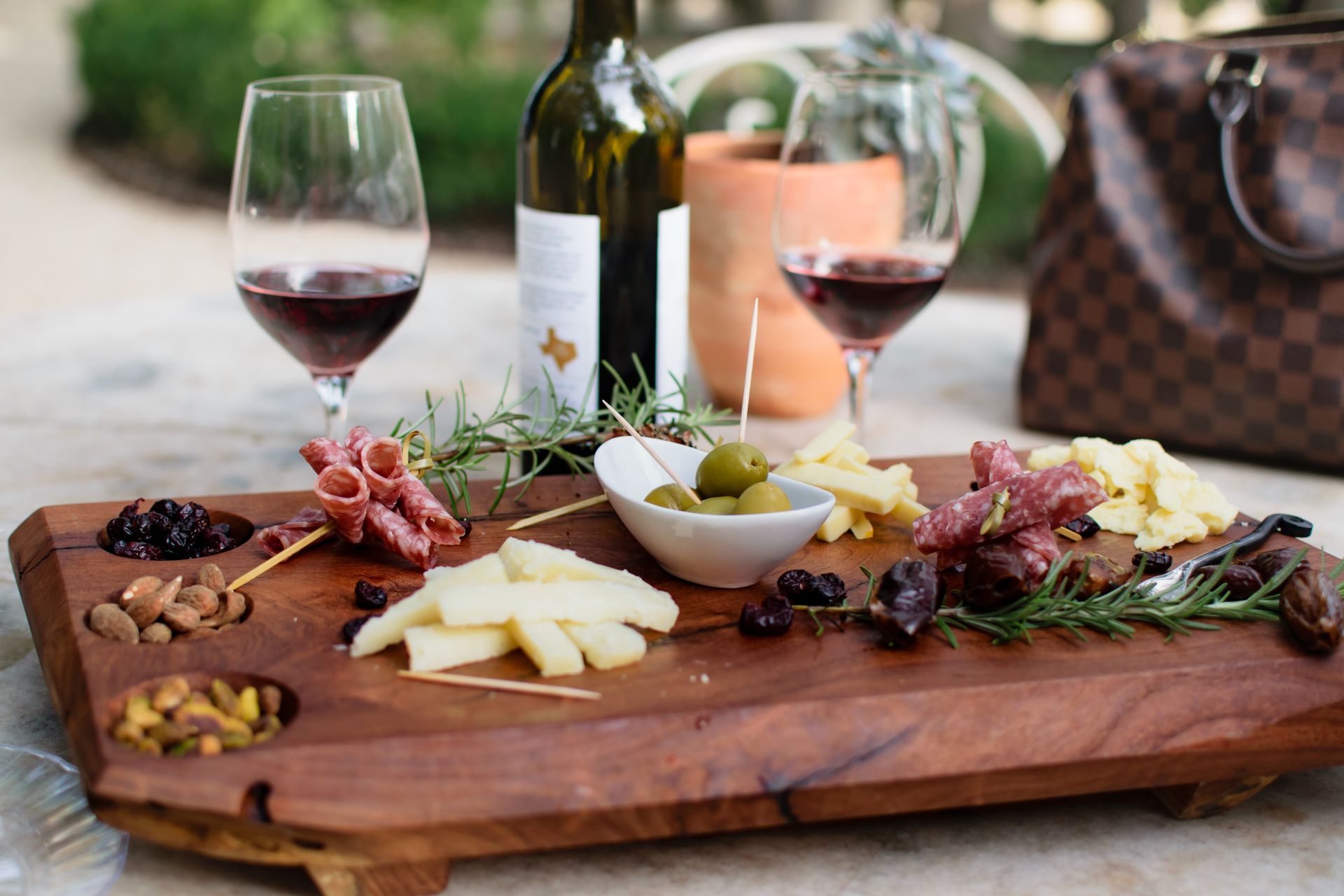 A wooden cutting board with a variety of food and wine glasses on it.