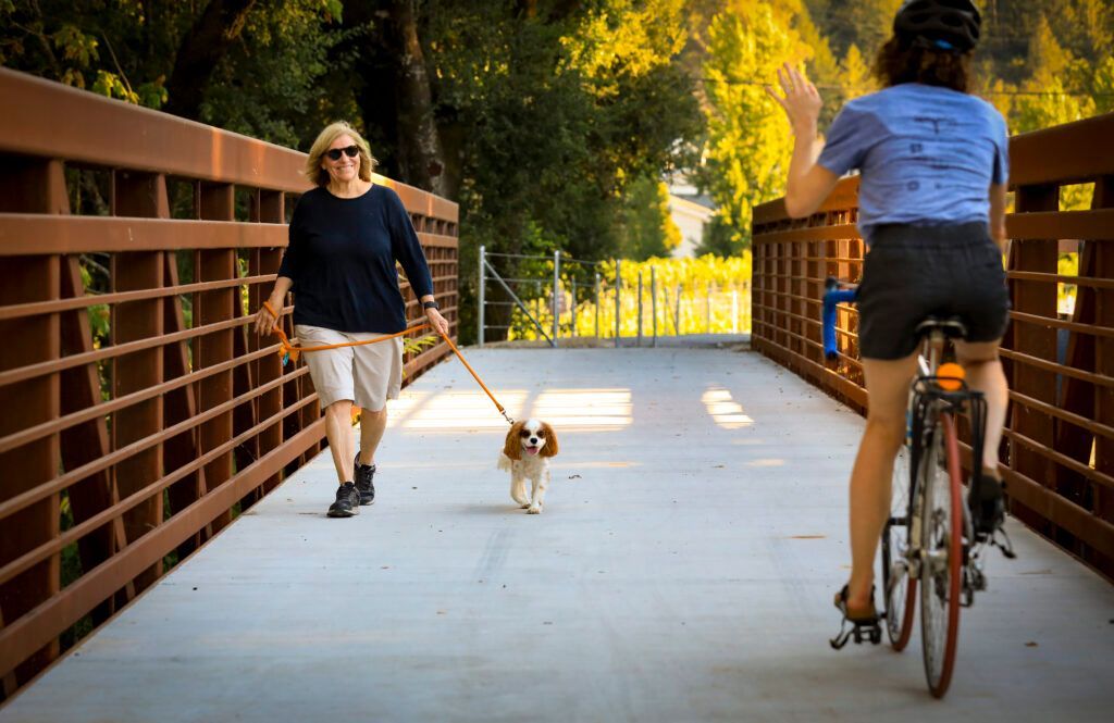 A woman is riding a bike while a man is walking a dog on a leash.