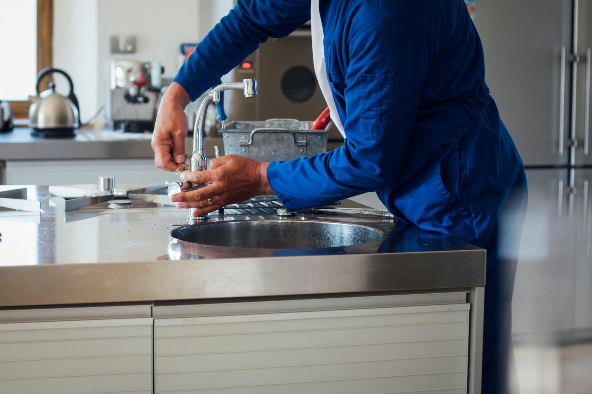Person in blue uniform washing hands at a stainless steel sink in a kitchen.