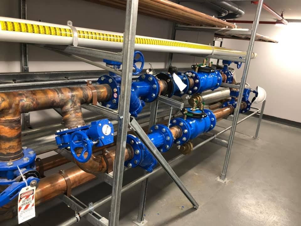 Blue valves and copper pipes in a utility room, mounted on a metal shelf.