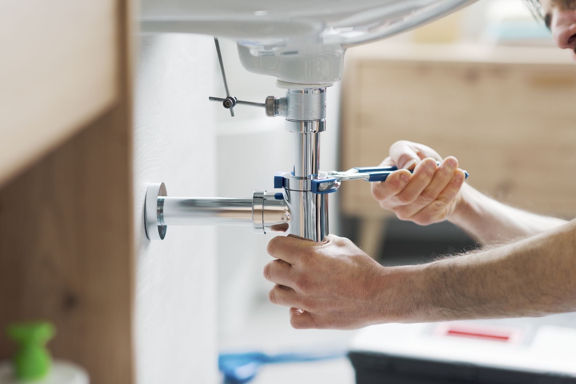 A man is fixing a sink pipe with a wrench.