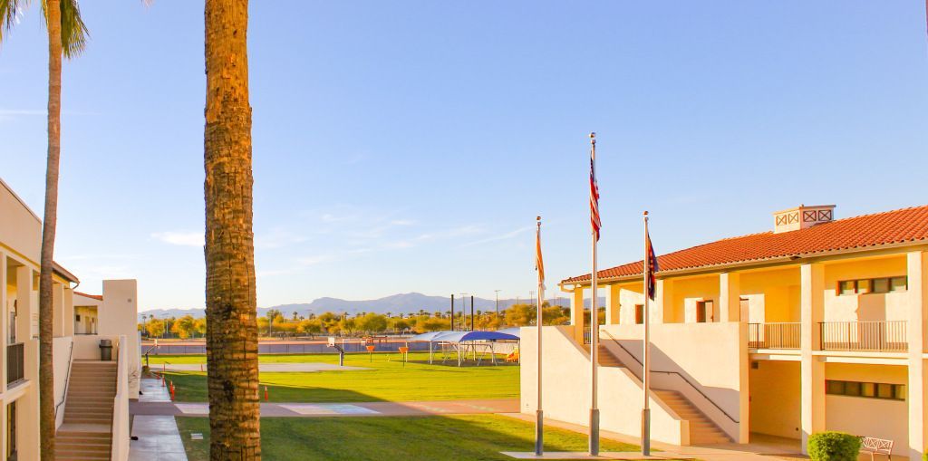 Sunny courtyard between beige buildings with palm trees, green lawn, and mountain view under a clear sky