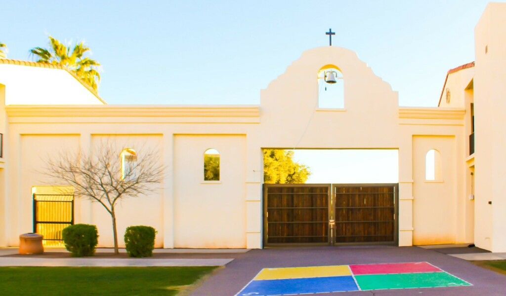 Modern white church facade with cross, wooden doors, and a rainbow-colored painted walkway in front