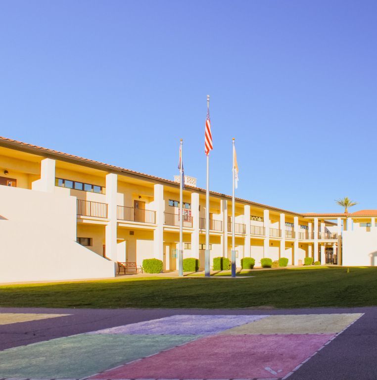 Sunny motel-style building with flags and a purple-painted crosswalk under a clear blue sky
