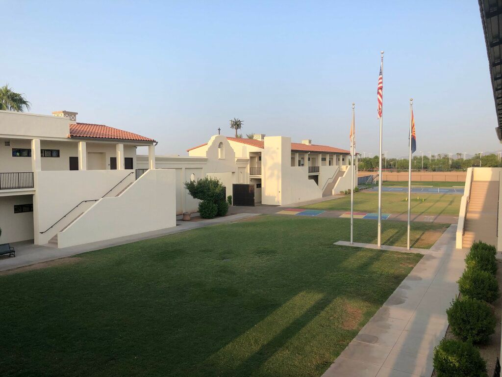 Courtyard with green lawn, white buildings, and flagpoles in front of a sunny campus.