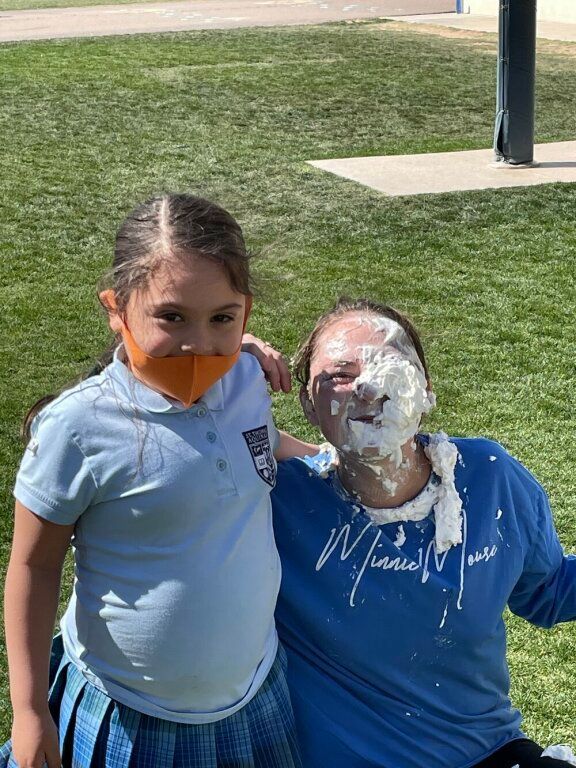 Two people outdoors; one has whipped cream on their face and shirt, both smiling.