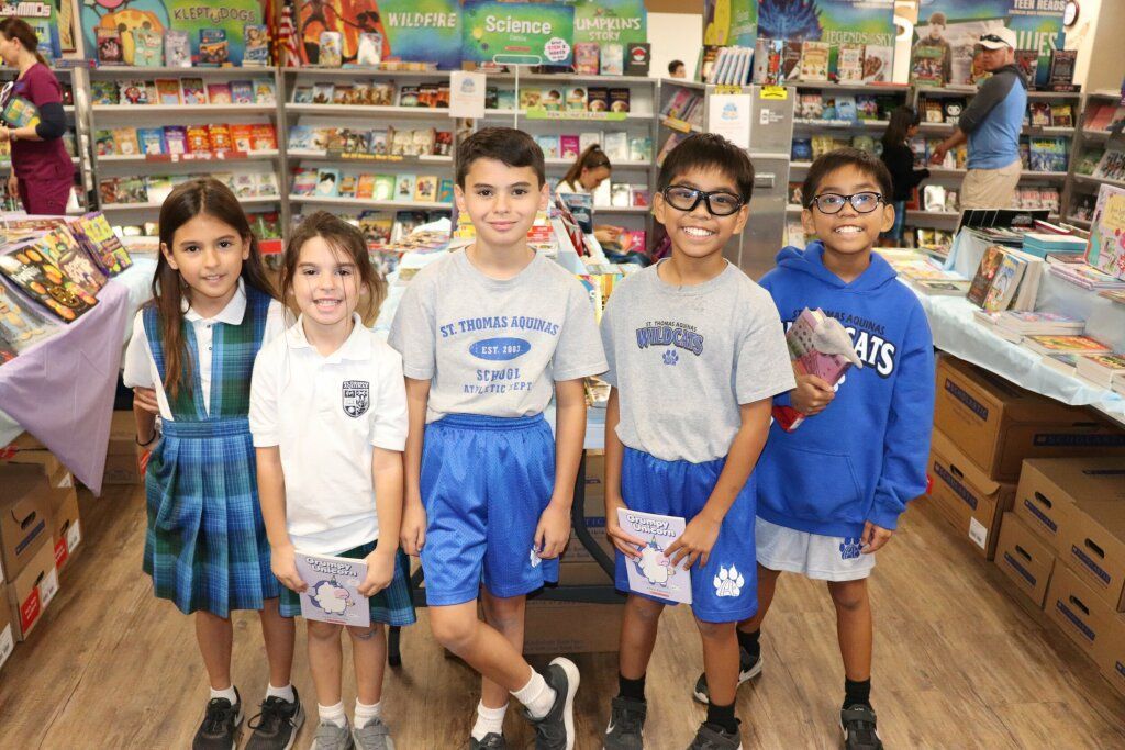 Five children standing in a store aisle, smiling in front of colorful shelves and tables.
