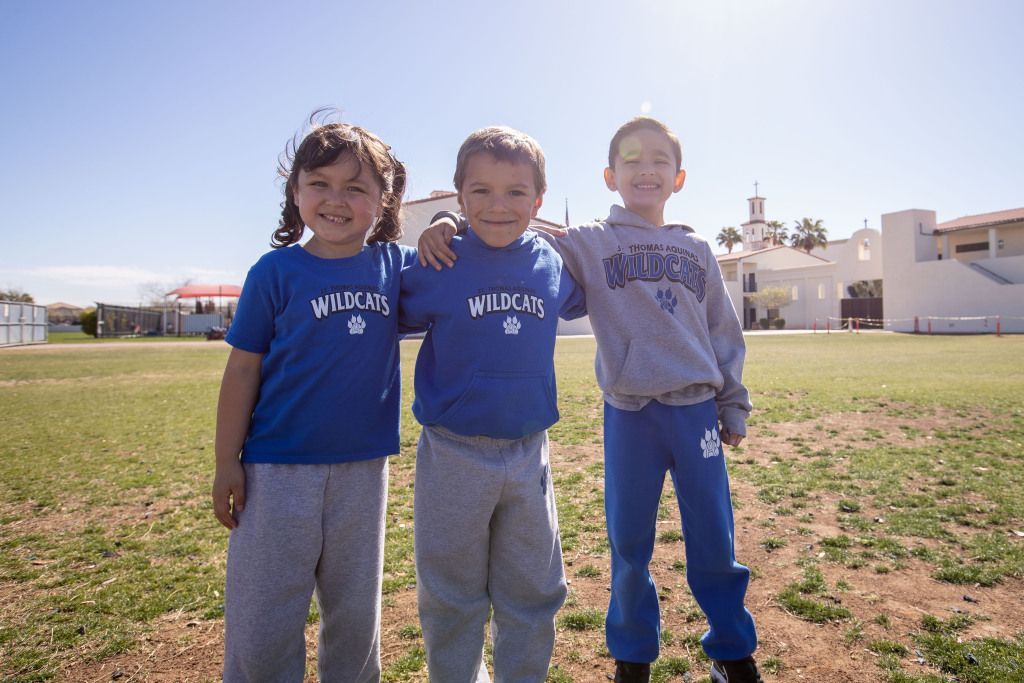 Three children stand arm in arm on a grassy field under bright sunlight.