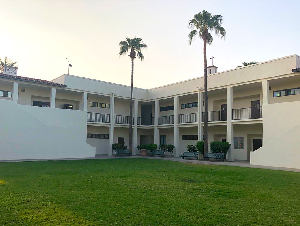 Courtyard of a white two-story building with balconies, green lawn, and tall palm trees at sunset