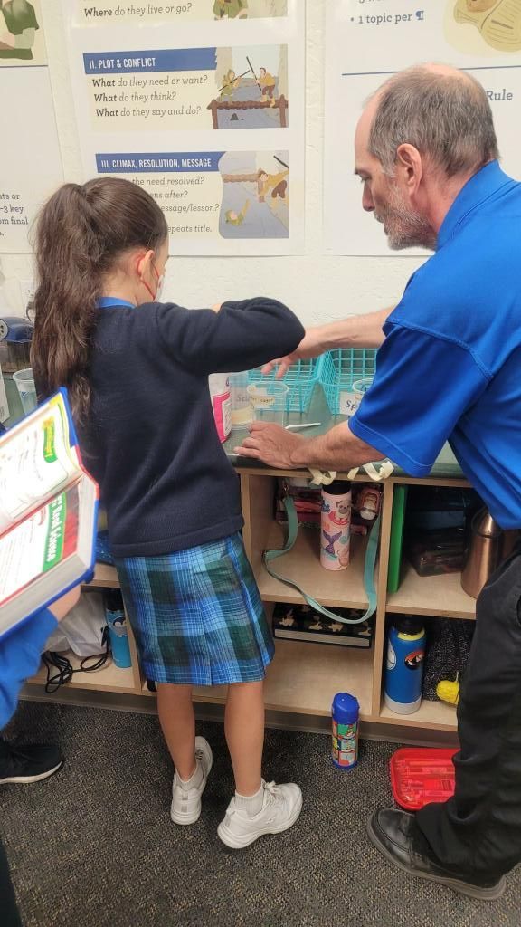 Teacher helping student sort classroom supplies at a shelf