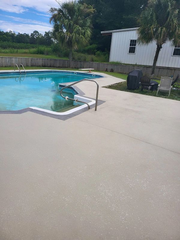 Poolside view: concrete deck, blue water, diving board, white building, green grass, palm trees, clear sky.