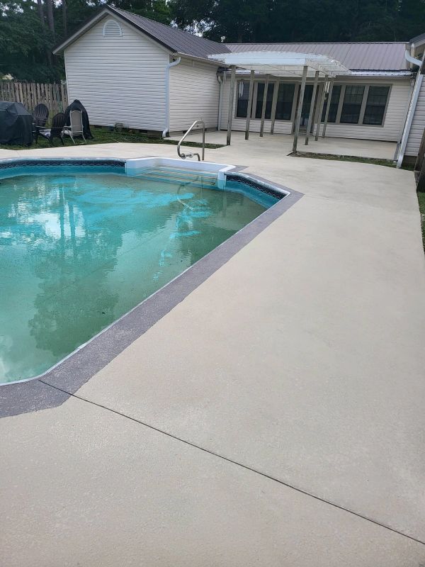 Pool and surrounding concrete patio in backyard, with a house in background.