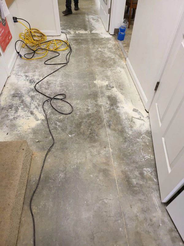 Bare cement hallway, with scattered debris. A coiled yellow extension cord and open doors are present.
