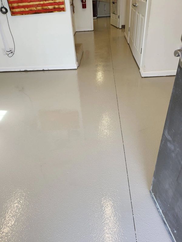Light gray, epoxy-coated floor in a hallway with white walls and a glimpse of a room.
