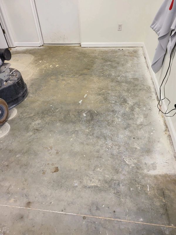 Concrete floor being worked on with a grinding machine in a room with white walls and trim.