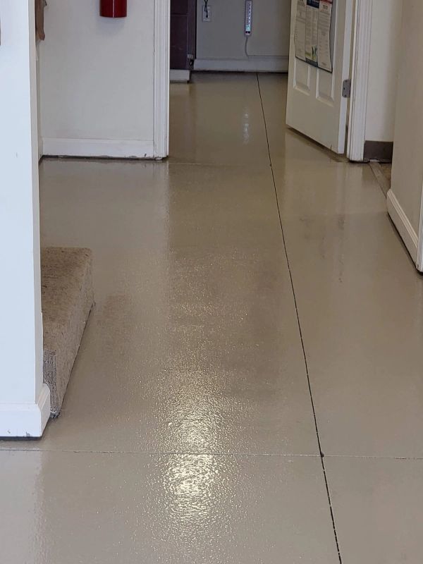 Hallway with shiny, light-colored floor, doorways on either side, and carpeted stairs visible on the left.