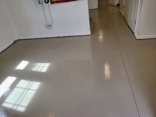 Gray, glossy epoxy floor in an interior hallway, reflecting sunlight. White walls and a doorway are also present.