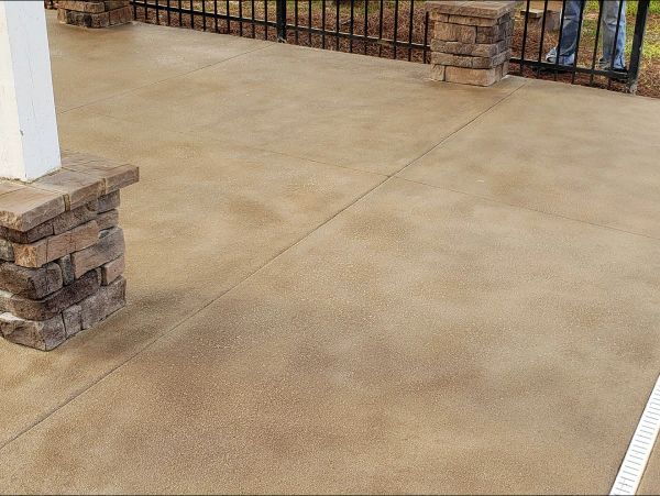 Tan-colored concrete patio with brown stone pillars and black wrought-iron fence.