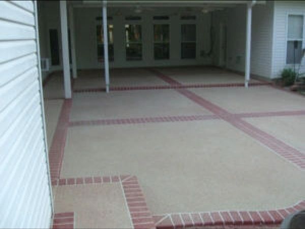 Concrete patio with red brick border. Covered area outside a house.