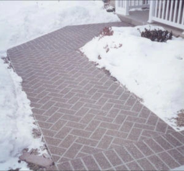 Brick walkway, partially covered in snow, leading to a house entrance.
