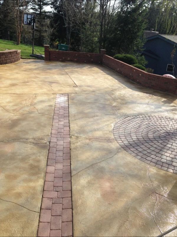Stamped concrete driveway with brick border and decorative circular pattern, bordered by a brick wall.
