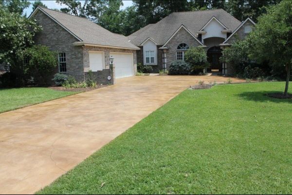 Brick house with stained driveway and green lawn.