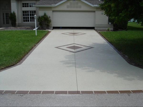 Cream-colored driveway with brick border and diamond-shaped tile accents, leading to a garage.