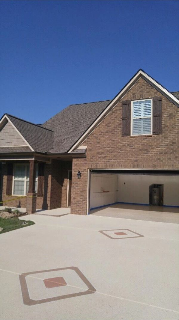A brick house with an open garage, brown shutters, and decorative squares on the driveway under a blue sky.