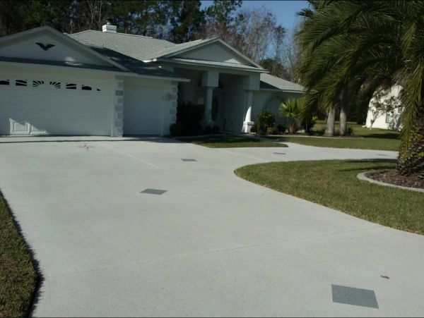 White house with gray roof and driveway, surrounded by green grass and palm tree.