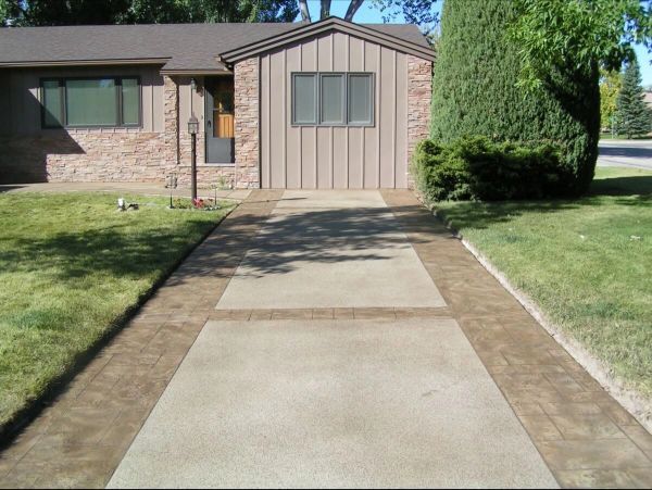 Driveway leading to a house with a green lawn, brown concrete border, and tan-colored concrete.