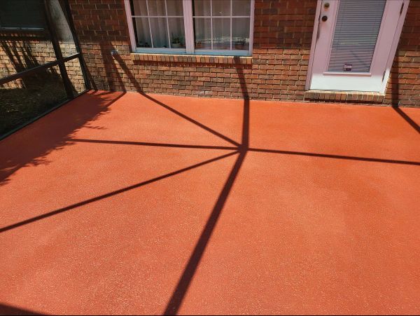 Red-painted patio floor with shadows cast by a structure against a brick wall and a window.