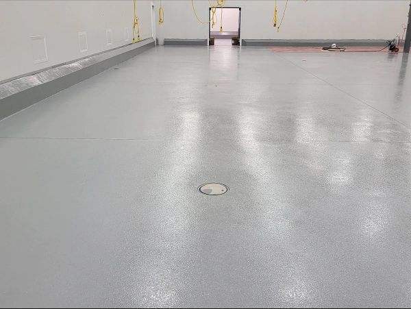 A gray, glossy epoxy floor in a clean, white-walled industrial space with a door at the end.