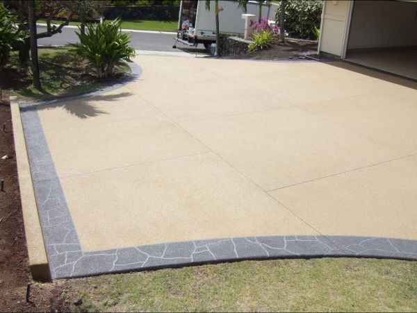 Beige concrete driveway with decorative gray stone border and open garage door.