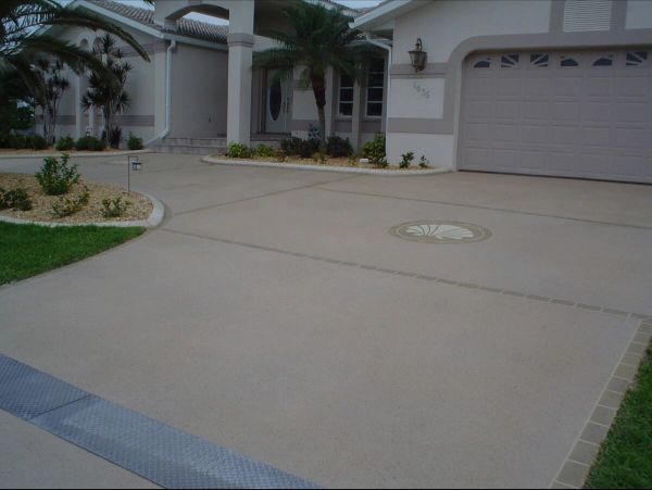 A concrete driveway leads to a house with a garage. The driveway is bordered by grass and landscaping.